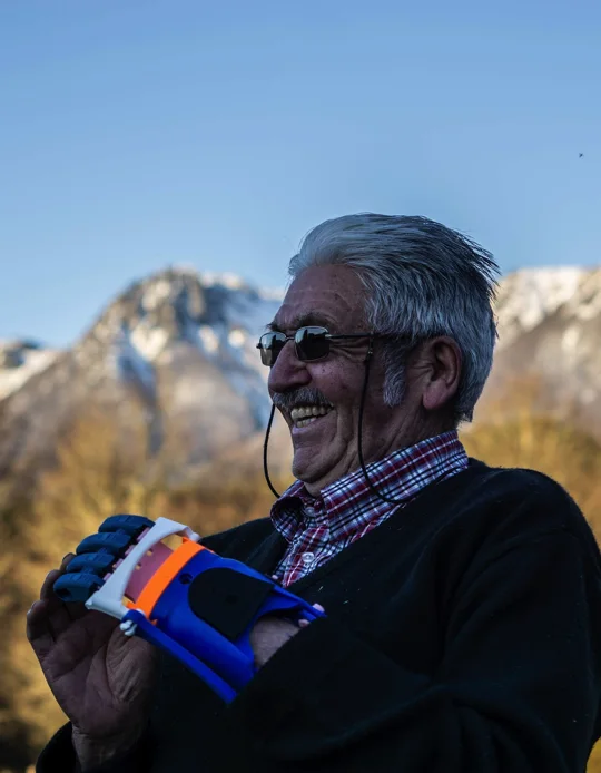 An adult wears a blue and orange 3D-printed prosthesis outdoors